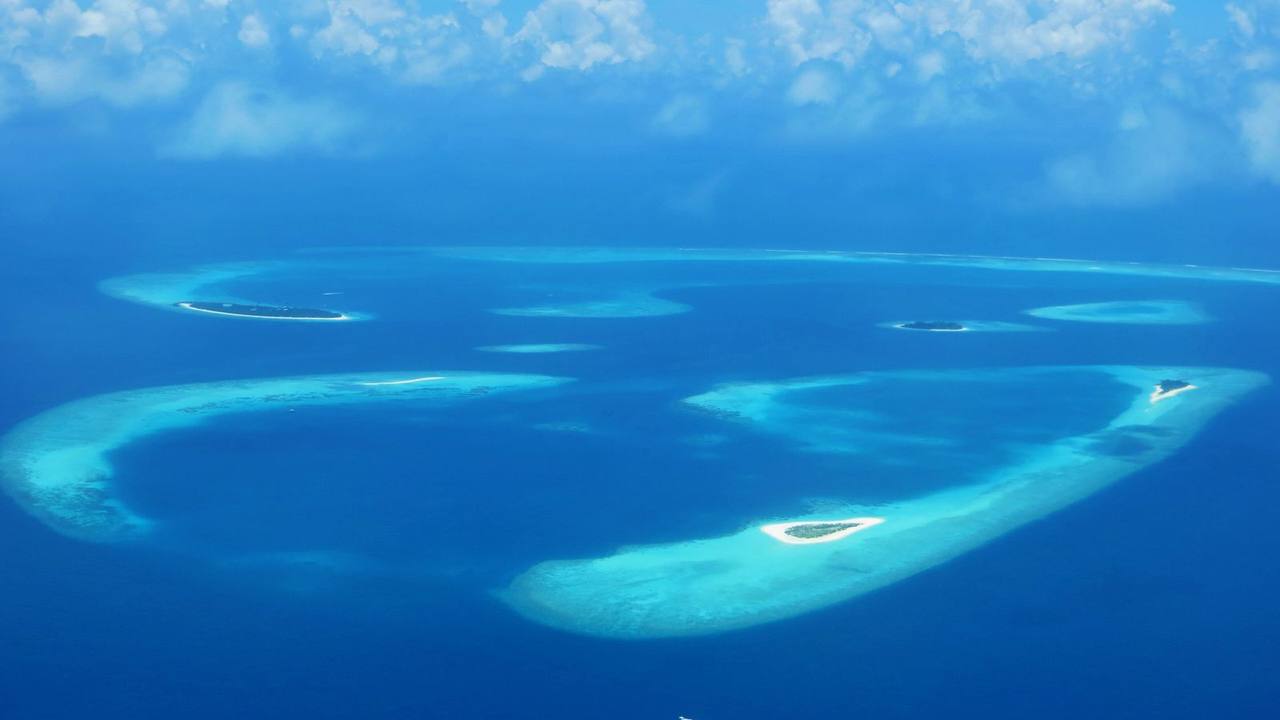Aerial view of a palm-covered island and turquoise lagoon in Baa Atoll, Maldives